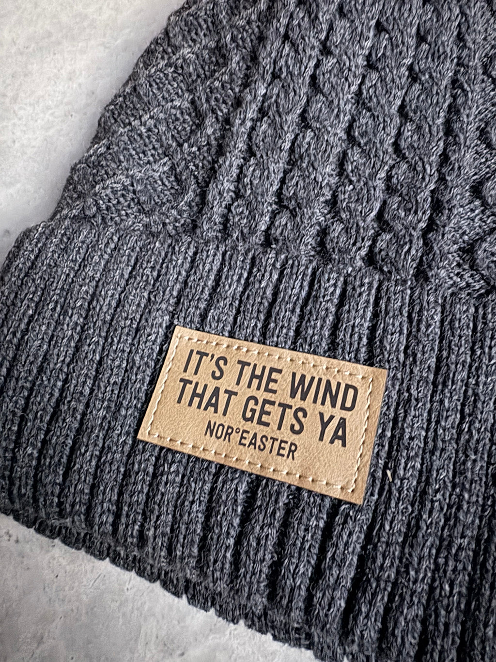 Gray knit beanie with a leather patch on a light gray background