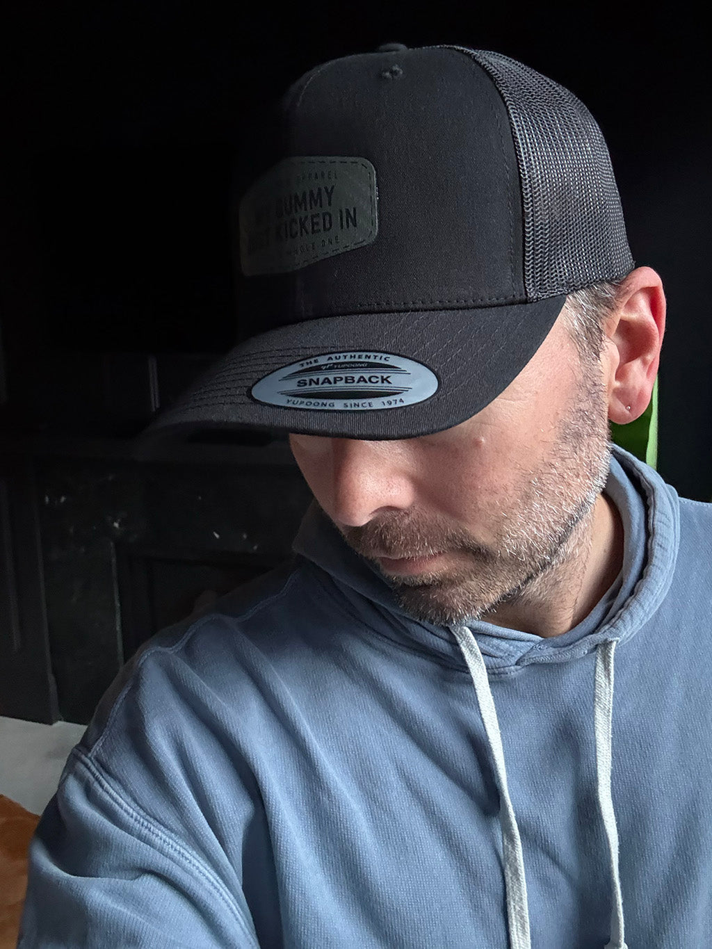 Person wearing a black cap with a brand logo and a gray hoodie.