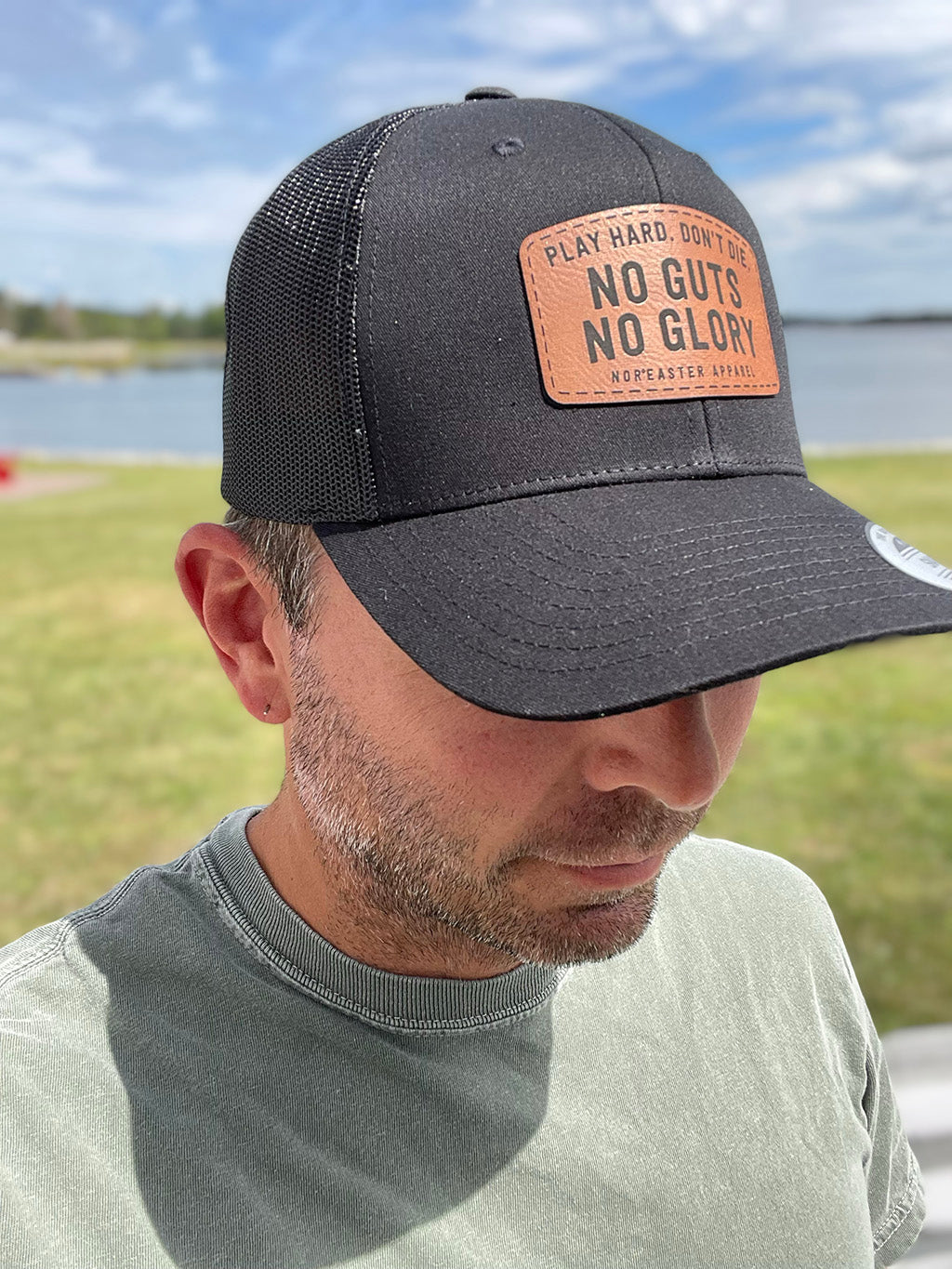 black nor'easter hat side view with a faux leather patch saying no guts no glory