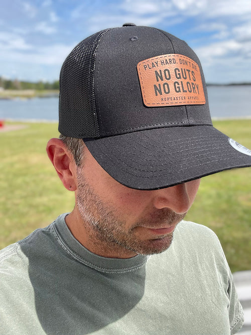 black nor'easter hat side view with a faux leather patch saying no guts no glory