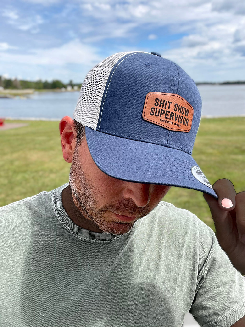 black nor'easter hat side view with a faux leather patch saying shit show supervisor