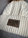 White knit beanie with a brown leather patch on a gray surface
