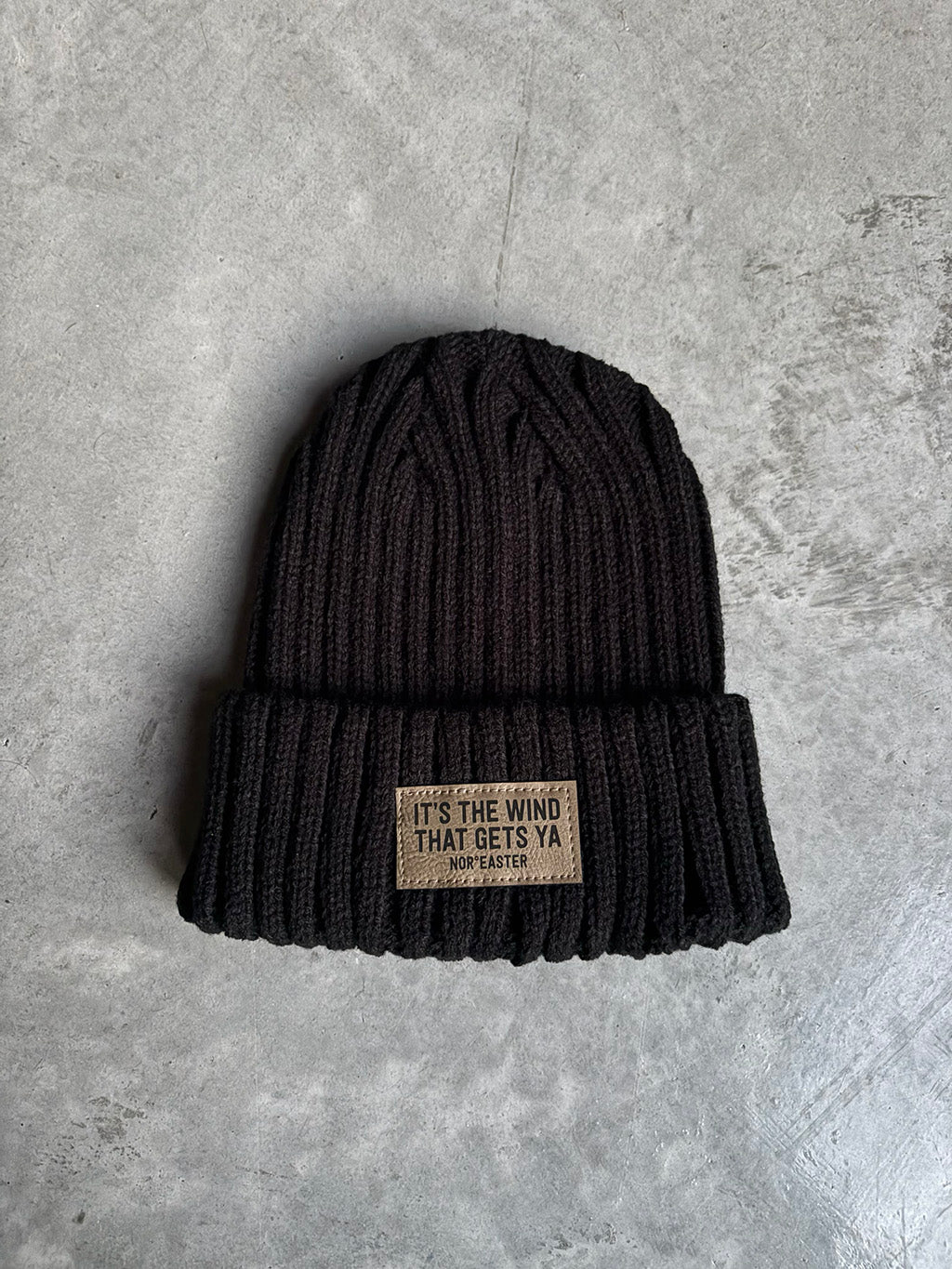 Black knit beanie with a label on a gray concrete surface