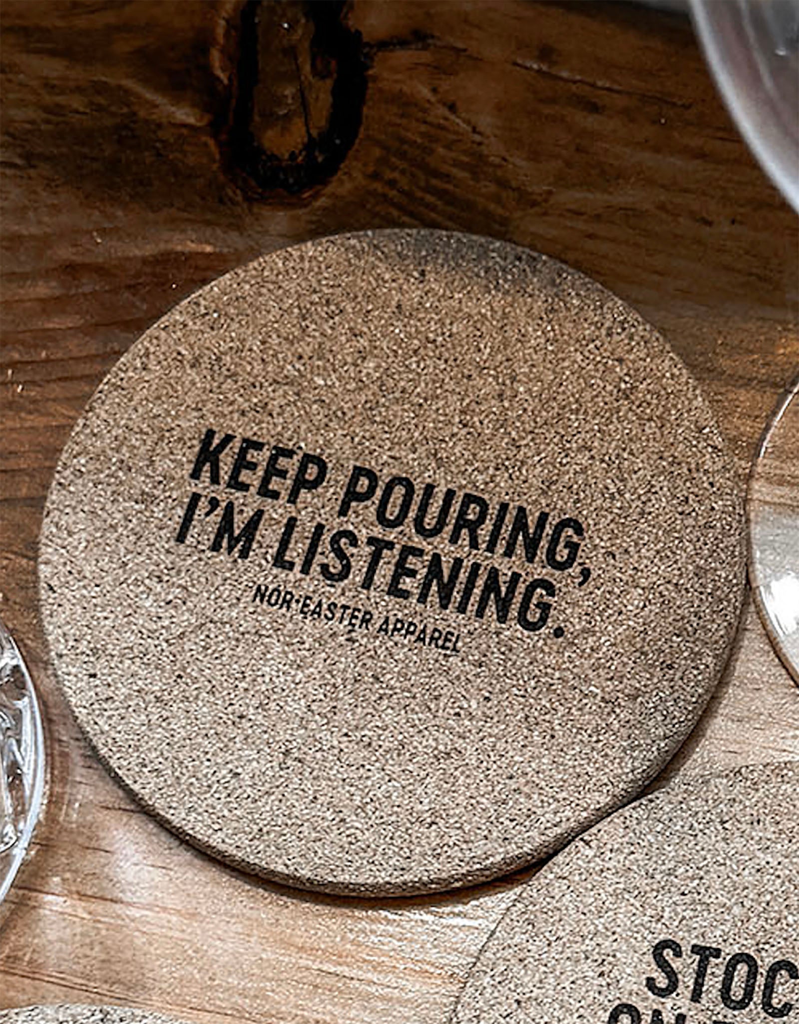 Cork coaster with 'Keep Pouring, I'm Listening' text on a wooden surface