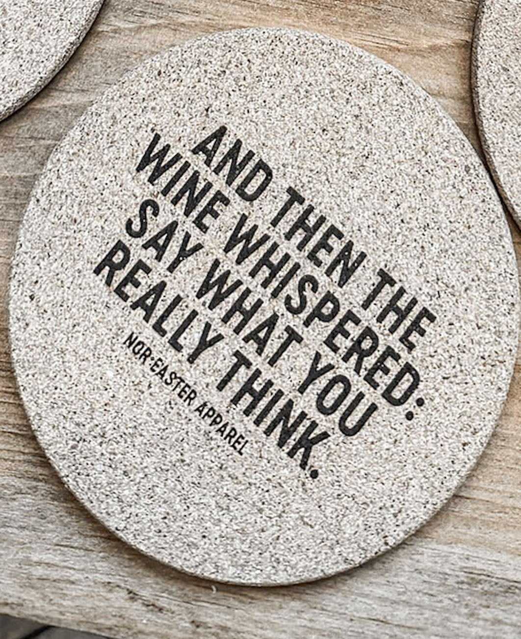 Round stone coaster with humorous text on a wooden surface