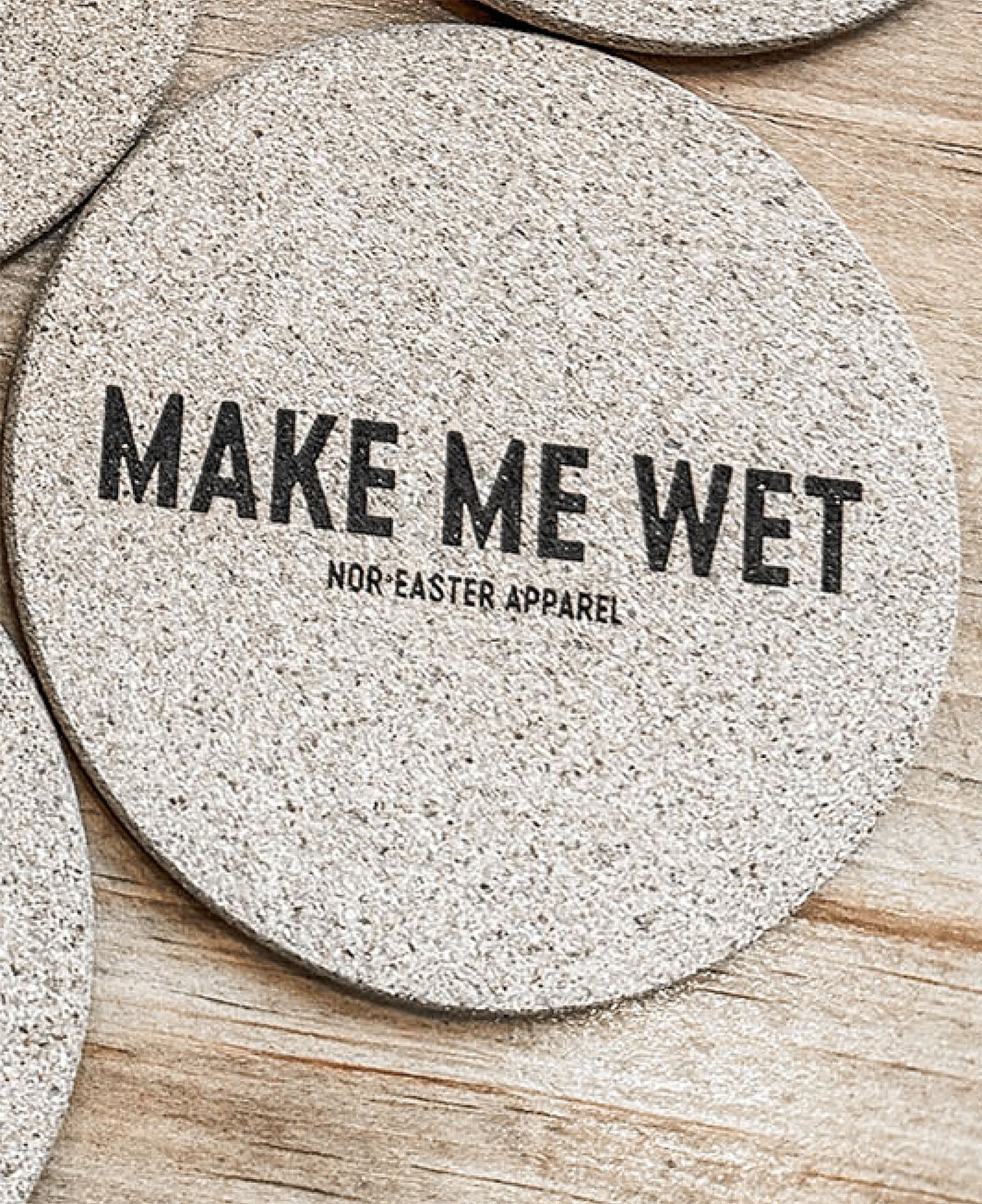Round stone coaster with 'MAKE ME WET' text on a wooden surface