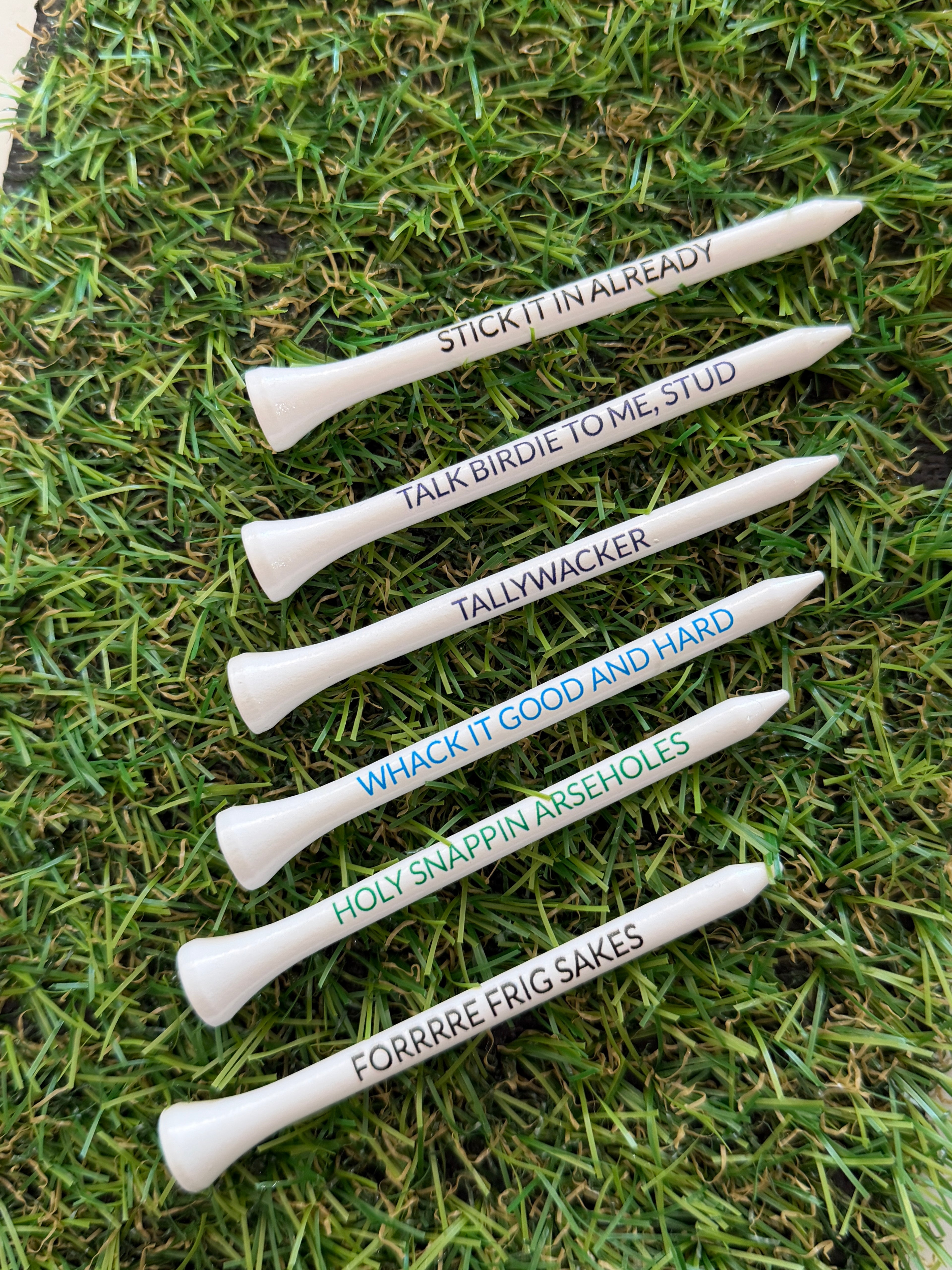 Set of six golf tees with humorous sayings on a grass background