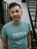 Man wearing a teal t-shirt with 'YHHHEA' text, standing indoors.
