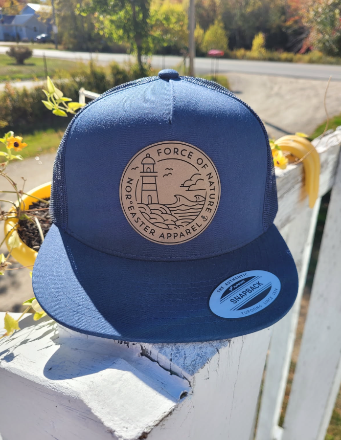 Force Of Nature Navy Trucker Hat front view on a railing with trees in the background