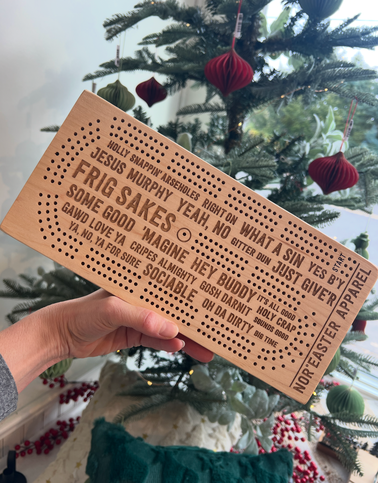 Person holding a wooden crib board with text in front of a decorated Christmas tree