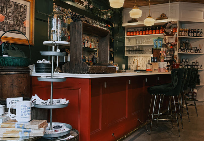 Bar area with red cabinets, shelves stocked with bottles, and a counter with various items.